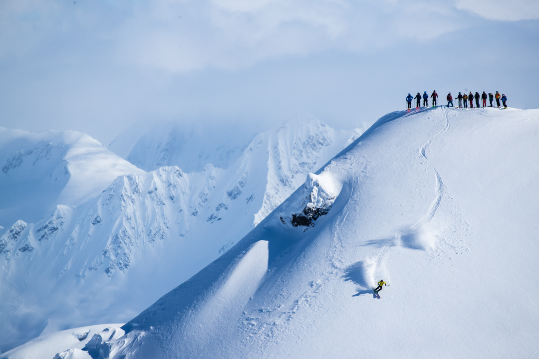 Friends watch as a skier drops in to a run in Alaska.